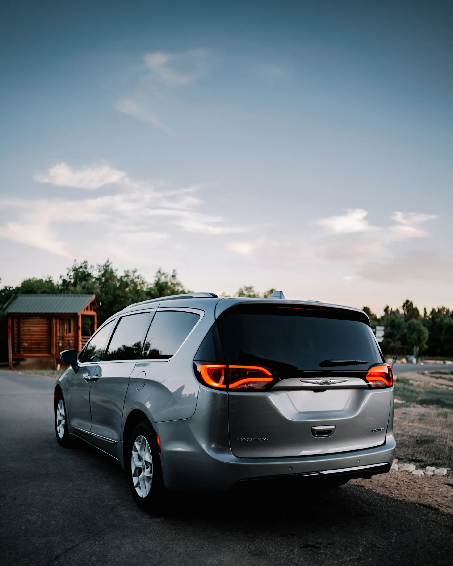 Silver Chrysler Pacifica parked on a road with rear lights illuminated.